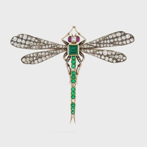 May include: A dragonfly brooch with a gold-tone body, emerald green and diamond accents. The wings are encrusted with diamonds. A square emerald is at the center of the body, with a ruby and diamond at the head.