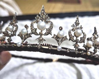 Puede incluir: Una tiara plateada ornamentada con perlas grandes y redondas y pequeñas gemas brillantes. La tiara tiene una banda de terciopelo oscuro y está diseñada con patrones simétricos intrincados. Un tocado lujoso para ocasiones especiales.