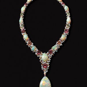 Può includere: Una lussuosa collana con un pendente a goccia di opale. La collana è adornata con varie pietre preziose, tra cui opali, tormaline rosa e piccoli diamanti bianchi. Le pietre preziose sono incastonate in un design delicato e ornato, creando un gioiello.