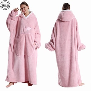 May include: A pink hooded blanket with a large front pocket and an apple design. The blanket has a white fleece lining in the hood and is designed to be worn. The image shows the front and back of the blanket.