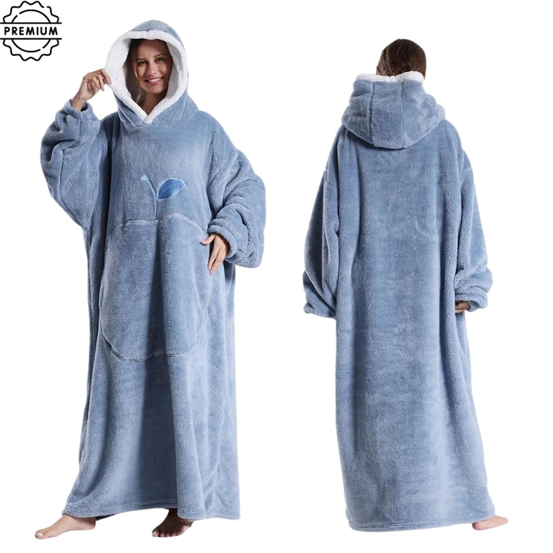 May include: A light blue, oversized wearable blanket with a hood and a large front pocket. The blanket has a soft, plush texture and a white lining in the hood. A small blue leaf design is on the front. The blanket is designed to be worn.