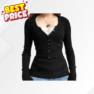May include: Black long-sleeve top with a scoop neckline and button-up front. The top has a ribbed texture and is paired with a white lace camisole. A gold-colored pendant necklace is visible. The image includes a "BEST PRICE" graphic.
