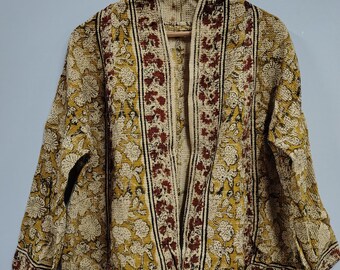 May include: A beige and yellow floral print jacket with a dark red and black border. The jacket is hanging on a wooden hanger against a light blue wall. The jacket has long sleeves and an open front.