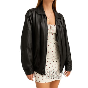 Könnte beinhalten: Schwarze Lederjacke mit Kragen und Knopfverschluss. Die Jacke wird über einem weißen Kleid mit rotem Tupfenmuster getragen. Das Bild ist vor einem weißen Hintergrund. Der Text "RIZION LEATHER" ist sichtbar.