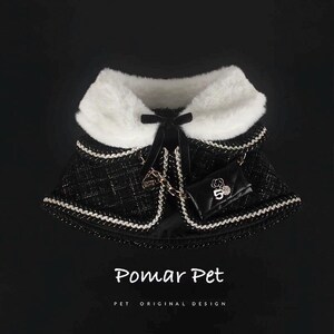 May include: A black and white dog cape with a faux fur collar and a small black purse. The cape has a quilted pattern with white trim and a black bow. The purse has a gold chain and the number 5.