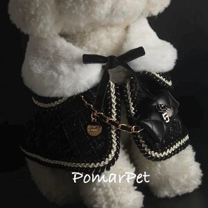 May include: A black and white dog jacket with a quilted design, gold chain, and a small purse. The jacket has a black bow and white trim. The text "PomarPet" is visible at the bottom.