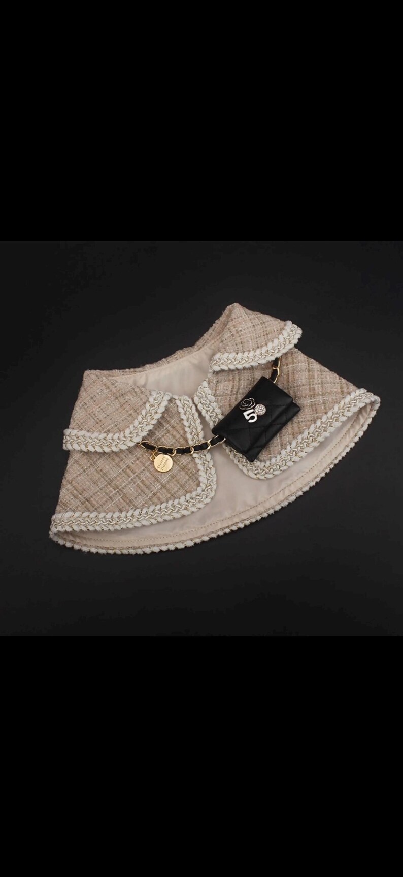 May include: A beige tweed dog jacket with white trim and a black chain. A small black quilted purse with a gold chain and the number 5 is attached to the jacket. A gold charm is also attached.