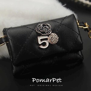 May include: Black quilted pet carrier with a gold chain strap. The carrier features a decorative black and white flower, the number 5, and a rhinestone embellishment. The text "PomarPet" is printed at the bottom.