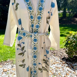 May include: A white waffle weave robe with a blue floral print and a matching blue sash. The robe has a V-neck and long sleeves.
