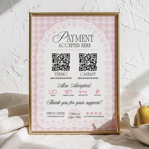 May include: A framed sign with a gold border displays "PAYMENT ACCEPTED HERE". The sign includes QR codes for Venmo and CashApp, along with accepted payment methods. The background is a pink gingham pattern with a lace border. The sign is on a white surface.