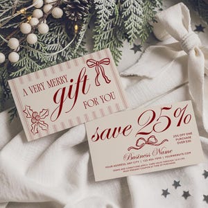 May include: Two holiday gift cards with red text and accents. One card reads "A very merry gift for you" and the other says "save 25%" with fine print. The cards are on a white cloth with greenery and a white bow.