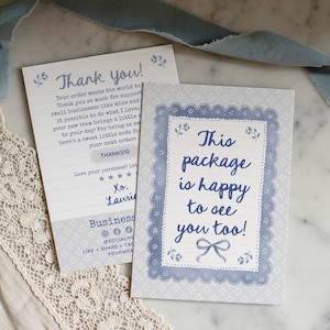 May include: Two light blue and white cards with text. One says "Thank You!" and the other says "This package is happy to see you too!" Both cards have a decorative border and floral accents. A blue ribbon and lace trim are also visible.