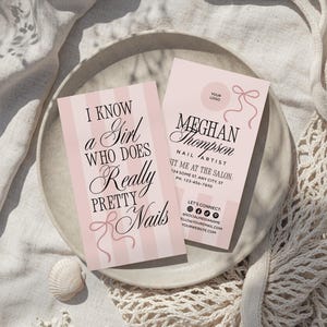 Peut inclure: Deux cartes de visite roses avec du texte et un motif de n&oelig;ud. L'une des cartes indique &laquo; Je connais une fille qui fait de tr&egrave;s jolis ongles &raquo;. L'autre carte indique &laquo; Meghan Thompson, Nail Artist &raquo; avec les coordonn&eacute;es et les ic&ocirc;nes des r&eacute;seaux sociaux.