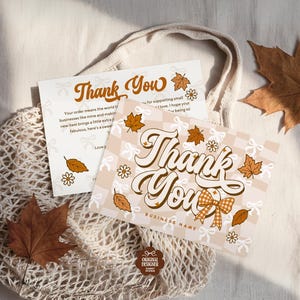 May include: Two "Thank You" cards with fall-themed designs, featuring brown leaves and floral accents. The cards are placed on a beige mesh bag, with two dried maple leaves. The cards have text that reads "Thank You" and "Business Name".