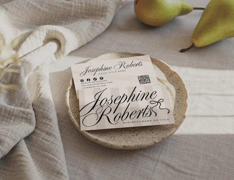 May include: A business card with the name "Josephine Roberts" in elegant script, resting on a speckled ceramic plate. The card features social media icons, a QR code, and space for a title and contact information. Two green pears are in the background.