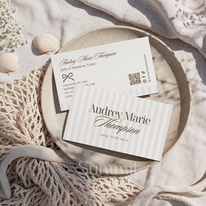 Puede incluir: Dos tarjetas de visita con el nombre "Audrey Marie Thompson" se muestran en un plato. Una tarjeta tiene rayas verticales y la otra un lazo. Las tarjetas incluyen informaci&oacute;n de contacto y redes sociales.