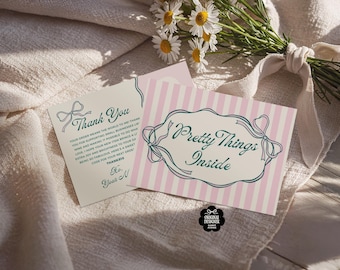 Puede incluir: Dos tarjetas de felicitación con texto e ilustraciones de lazo. Una tarjeta dice "Thank You" y la otra "Pretty Things Inside" sobre un fondo a rayas rosas. Un ramo de margaritas y un paño de lino están en el fondo.