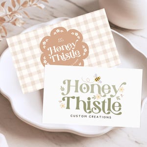 May include: Two business cards with a light brown gingham pattern and a green and yellow logo that says "Honey Thistle Custom Creations".