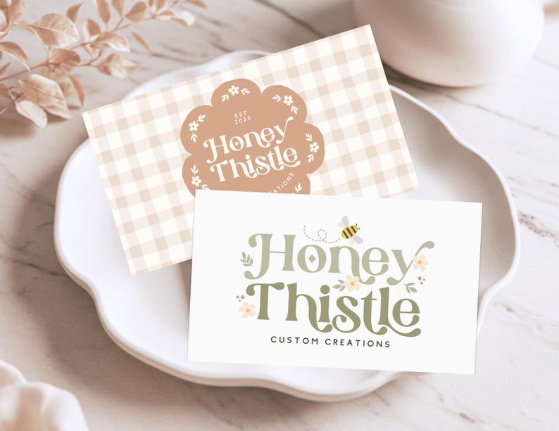 May include: Two business cards with a light brown gingham pattern and a green and yellow logo that says "Honey Thistle Custom Creations".