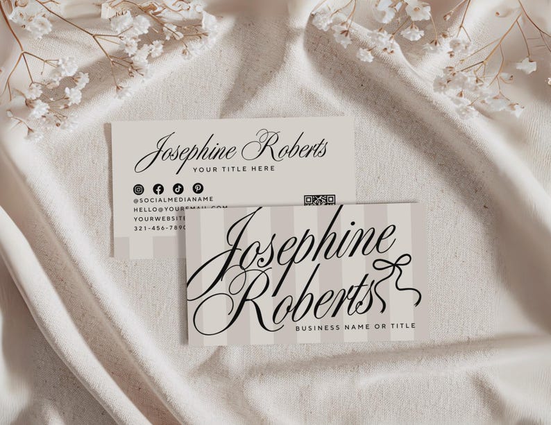 May include: Two business cards with the name "Josephine Roberts" in elegant script. One card has a vertical striped background and the other has social media icons and contact information. The cards are on a white fabric surface.