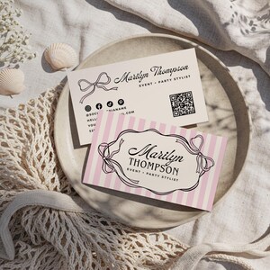 May include: Two business cards with the name "Marilyn Thompson" and the title "Event + Party Stylist". One card has pink and white stripes, the other is plain. Both cards have a bow design and social media icons.