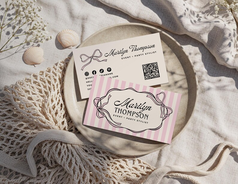 May include: Two business cards with the name "Marilyn Thompson" and the title "Event + Party Stylist". One card has pink and white stripes, the other is plain. Both cards have a bow design and social media icons.
