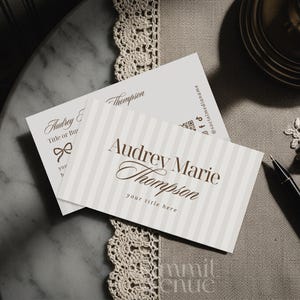 Puede incluir: Dos tarjetas de visita con el nombre "Audrey Marie Thompson" en escritura elegante. Una tarjeta tiene un fondo a rayas, la otra un lazo. Tambi&eacute;n se ven un bol&iacute;grafo negro y accesorios dorados.