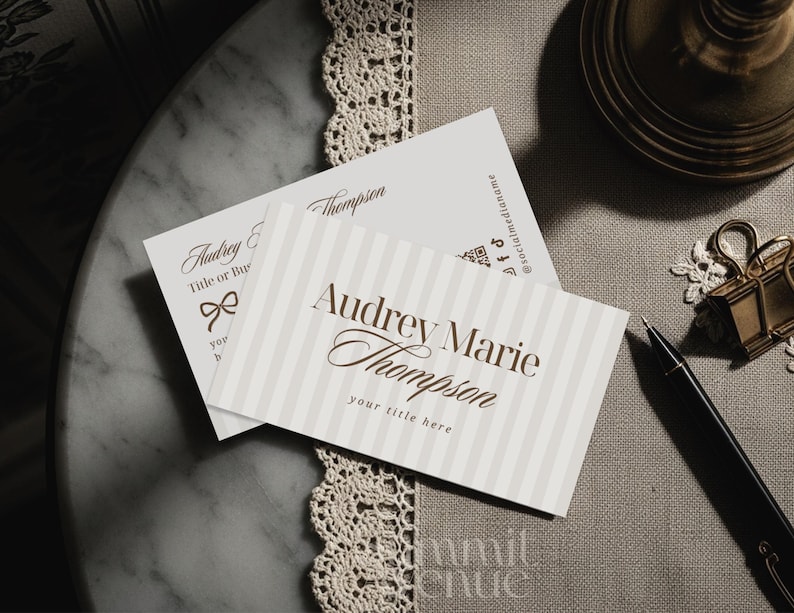 Puede incluir: Dos tarjetas de visita con el nombre "Audrey Marie Thompson" en escritura elegante. Una tarjeta tiene un fondo a rayas, la otra un lazo. Tambi&eacute;n se ven un bol&iacute;grafo negro y accesorios dorados.
