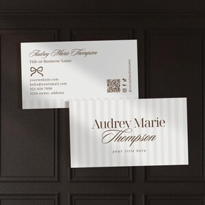 Puede incluir: Dos tarjetas de visita con el nombre "Audrey Marie Thompson". Una tarjeta tiene un lazo y datos de contacto. La otra tiene rayas verticales y el texto "your title here".