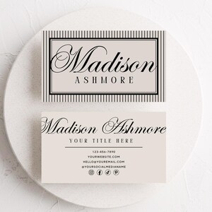 May include: Two business cards with the name "Madison Ashmore" in elegant script. One card features a striped border and the name, while the other includes contact information and social media icons. The cards are light beige.