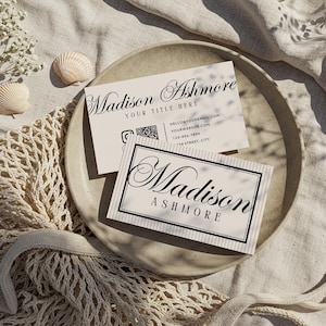 Pu&ograve; includere: Due biglietti da visita con il nome "Madison Ashmore" in elegante scrittura sono esposti su un piatto beige. Un biglietto ha un bordo nero e gessati. L'altro biglietto ha informazioni di contatto.