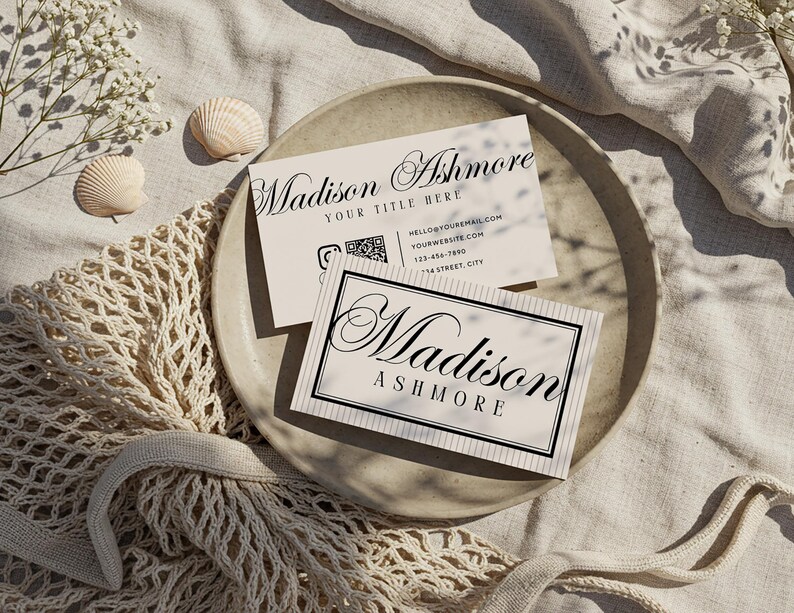 Pu&ograve; includere: Due biglietti da visita con il nome "Madison Ashmore" in elegante scrittura sono esposti su un piatto beige. Un biglietto ha un bordo nero e gessati. L'altro biglietto ha informazioni di contatto.