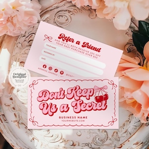 May include: Two pink referral cards with red text and a retro design. One card reads "Refer a Friend" and the other says "Don't Keep Us a Secret". The cards are decorated with cherries and bows, and are surrounded by pink flowers.