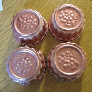 May include: Four copper-colored metal molds for making desserts. Each mold has a fluted edge and a raised design of a bunch of grapes.