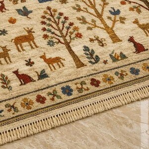 Pu&ograve; includere: Tappeto beige con un motivo ripetuto di alberi, cervi ed elementi floreali nei toni del marrone, rosso, blu e giallo. Il tappeto ha un bordo con frange e un bordo con disegni floreali e geometrici. Lo stile &egrave; rustico e decorativo.