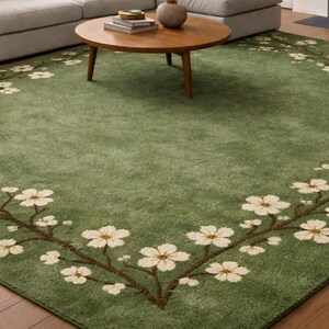 Puede incluir: Una alfombra verde con un dise&ntilde;o floral. La alfombra presenta un borde de ramas marrones con flores blancas. La alfombra es rectangular y est&aacute; colocada en un sal&oacute;n.