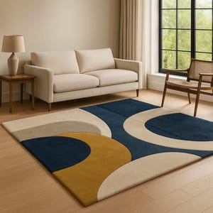 May include: A rectangular area rug with a modern design. The rug features a pattern of overlapping shapes in navy blue, mustard yellow, and beige. The rug is placed on a hardwood floor in a living room setting.