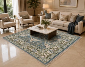Può includere: Un grande tappeto rettangolare con un campo centrale blu e un bordo dettagliato. Il tappeto presenta un design tradizionale con motivi floreali e geometrici nei toni del blu, verde e crema. Il tappeto ha un bordo sfrangiato ed è posto in un soggiorno.