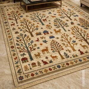 Pu&ograve; includere: Tappeto beige con un motivo ripetuto di alberi, cervi, uccelli e piccole case. Gli alberi hanno tronchi marroni e foglie colorate. Il tappeto ha un bordo decorativo con elementi floreali e geometrici e un bordo con frange.