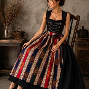 May include: A black sleeveless bodice featuring silver-toned decorative chains and buttons, paired with a long, full skirt. The skirt displays vertical panels of solid black alternating with patterned stripes in red, navy blue, and cream with ornate motifs.