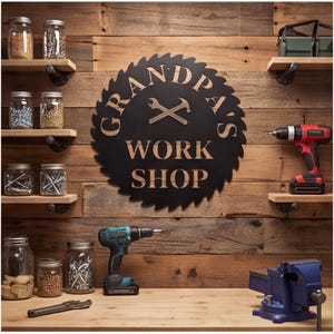 Könnte beinhalten: Ein rundes, schwarzes Wandschild aus Metall in Form eines Sägeblatts mit dem Text GRANDPA'S WORK SHOP und einem Symbol aus gekreuztem Schraubenschlüssel und Hammer. Das Schild hängt an einer Holzwand mit Regalen, Gläsern und Werkzeugen.