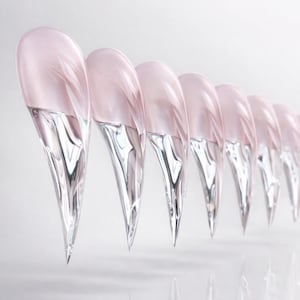 May include: A row of eight clear, teardrop-shaped objects with a pinkish hue at the top and a transparent, crystalline lower portion. The objects are arranged in a line, with their pointed ends facing downward.
