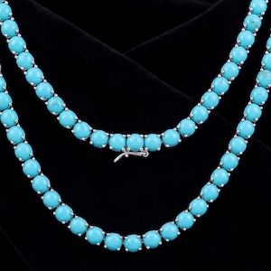 Könnte beinhalten: Zwei Stränge Türkisperlenketten mit einem silbernen Verschluss. Die Perlen sind leuchtend hellblau und gleichmäßig angeordnet. Der Hintergrund ist ein dunkler, samtiger Stoff.