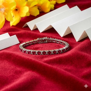 Könnte beinhalten: Ein silbernes Armband mit rechteckigen roten Edelsteinen und kleinen weißen Akzentsteinen. Das Armband liegt auf rotem Samt, mit gelben Blumen und weißen Papierakzenten im Hintergrund.