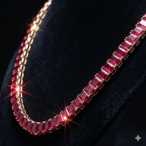 Könnte beinhalten: Eine goldfarbene Halskette mit einer Reihe rechteckiger, tiefroter Edelsteine. Die Edelsteine sind eng aneinander gesetzt und bilden eine durchgehende Farblinie. Die Halskette wird vor einem dunklen Hintergrund präsentiert, der ihr Funkeln hervorhebt.