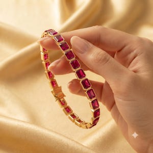 Peut inclure: Un bracelet doré composé d'une rangée continue de pierres rectangulaires facettées rose foncé serties dans des cadres métalliques. Le bracelet comprend un mécanisme de fermoir métallique sécurisé et une structure à maillons flexibles.
