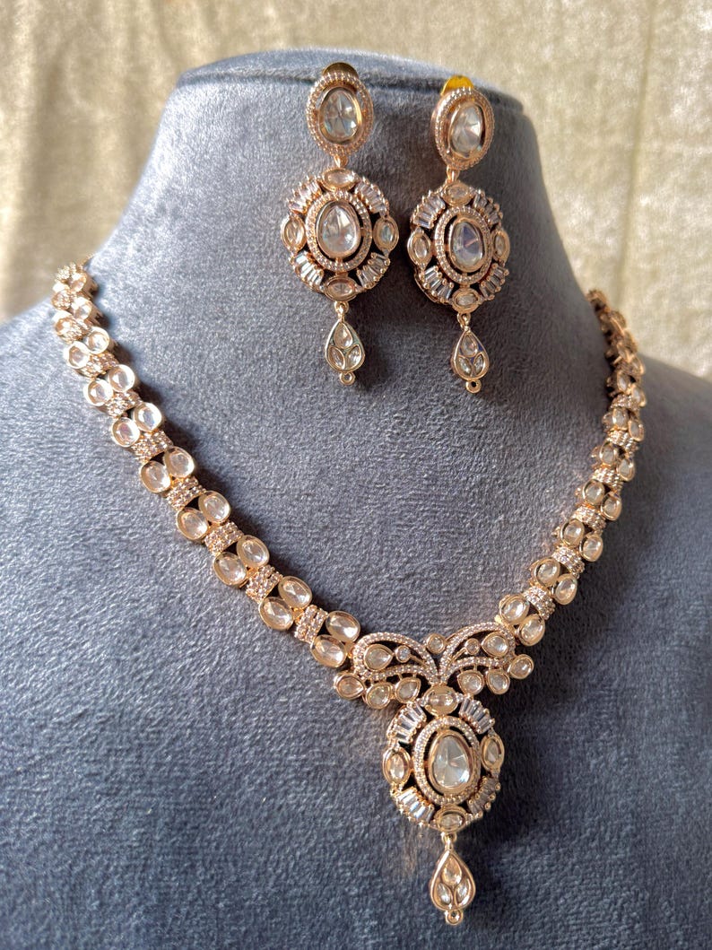 K&ouml;nnte beinhalten: Ein Set aus ros&eacute;goldener Halskette und passenden Ohrringen. Die Halskette hat einen ovalen Mittelanh&auml;nger mit einem tropfenf&ouml;rmigen Anh&auml;nger. Die Ohrringe haben ein &auml;hnliches Design, mit einem gro&szlig;en Mittelstein und einem Tropfen. Der Schmuck ist mit klaren Steinen besetzt.