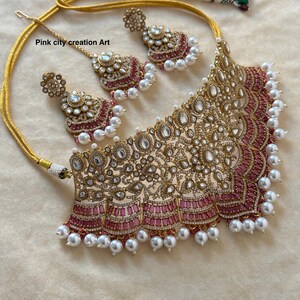 May include: A gold-toned necklace and earring set with a matching headpiece. The jewelry features clear and pink gemstones, and white pearls. The necklace has a wide, ornate design with a pink border. The text "Pink city creation Art" is visible.