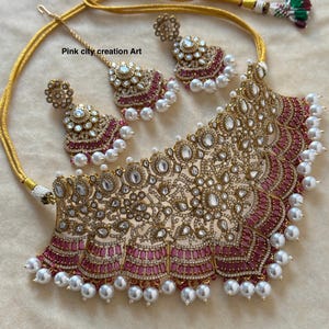 May include: A gold-toned necklace and earring set with a matching headpiece. The jewelry features clear and pink gemstones, and white pearls. The text "Pink city creation Art" is visible on the image.