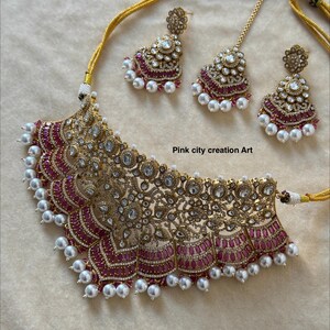 May include: A gold-toned necklace and earring set with a matching headpiece. The necklace and earrings feature intricate detailing with clear and pink gemstones, and white pearls. The text "Pink city creation Art" is visible.